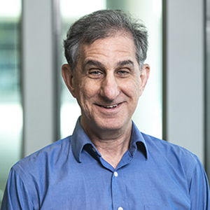 A man in a blue collared shirt stands outside and smiles